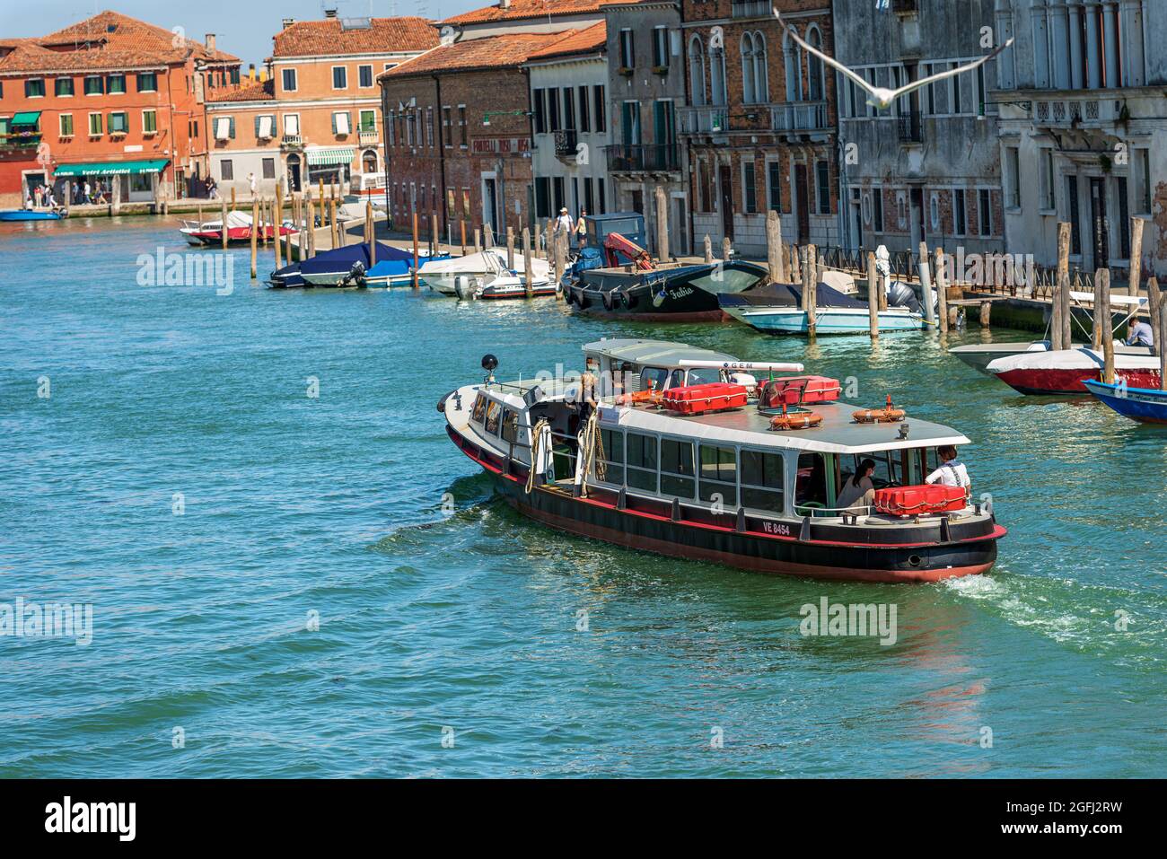 Actv (municipal company for public transport) Ferry Boat or Vaporetto with tourists in motion in a canal of the Murano island, Venice, Italy. Stock Photo
