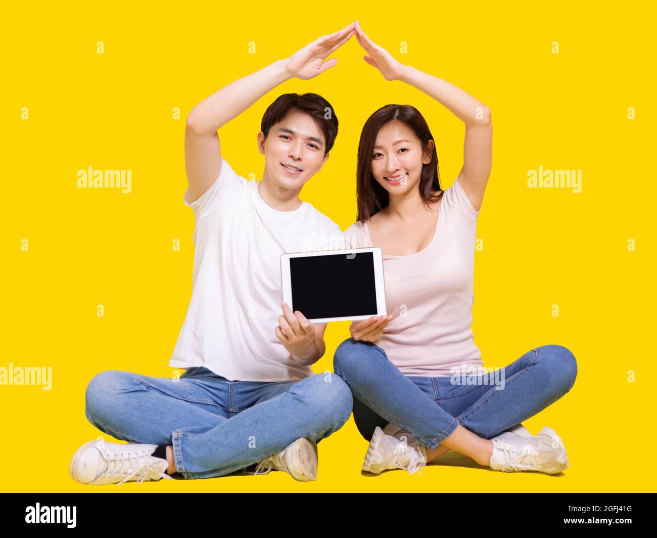 Young happy couple with roof house hand gesture and tablet.Isolated on yellow background. Stock Photo