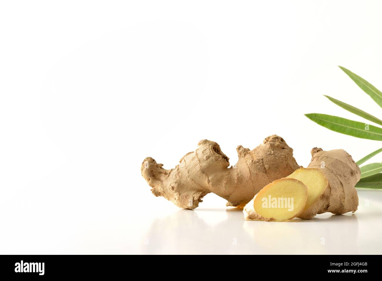 Ginger root with sliced portions and leaves behind with white isolated background reflected on white table Stock Photo