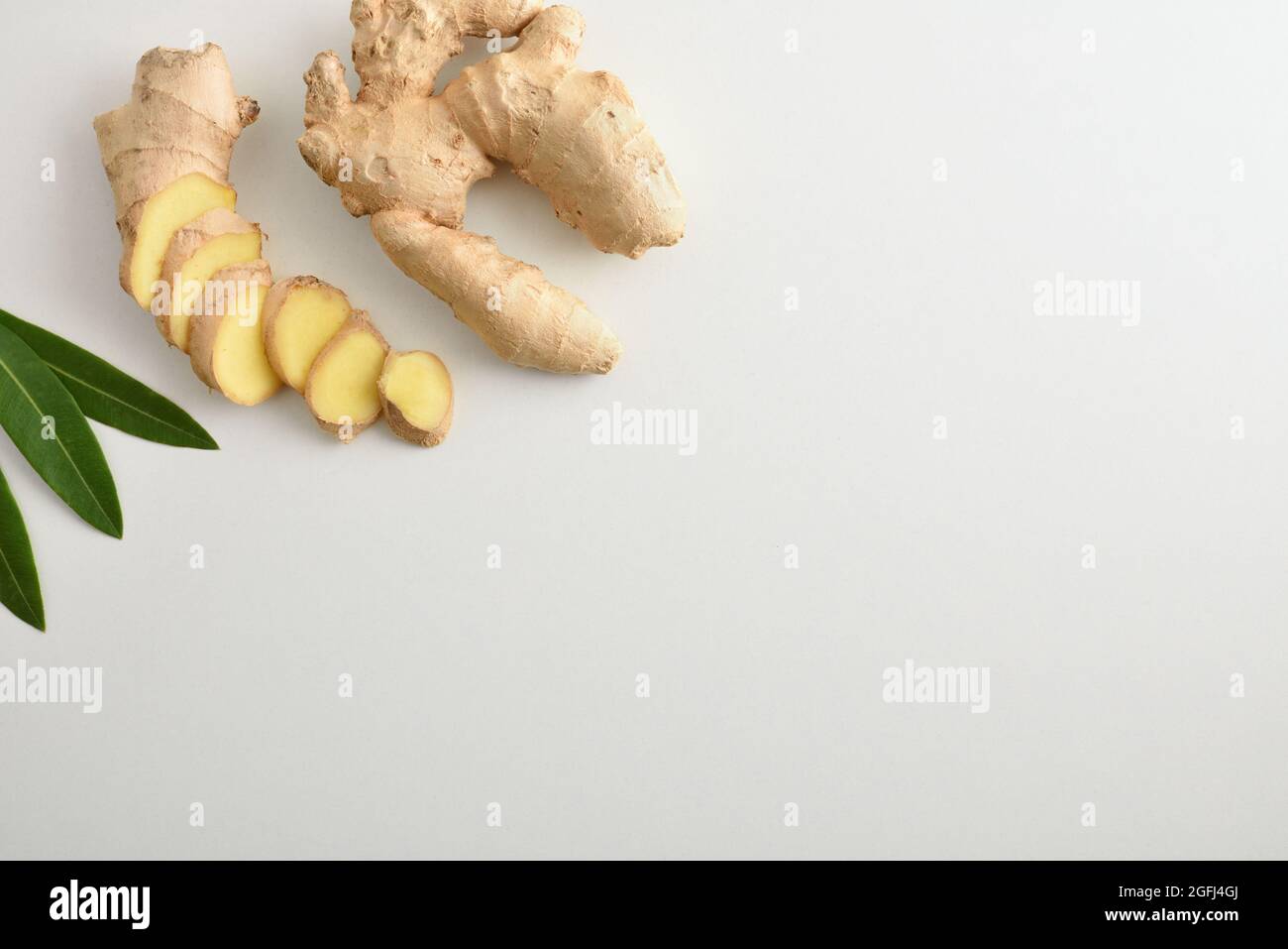 Fresh ginger root with sliced portions on white table and leaves. Top view. Stock Photo