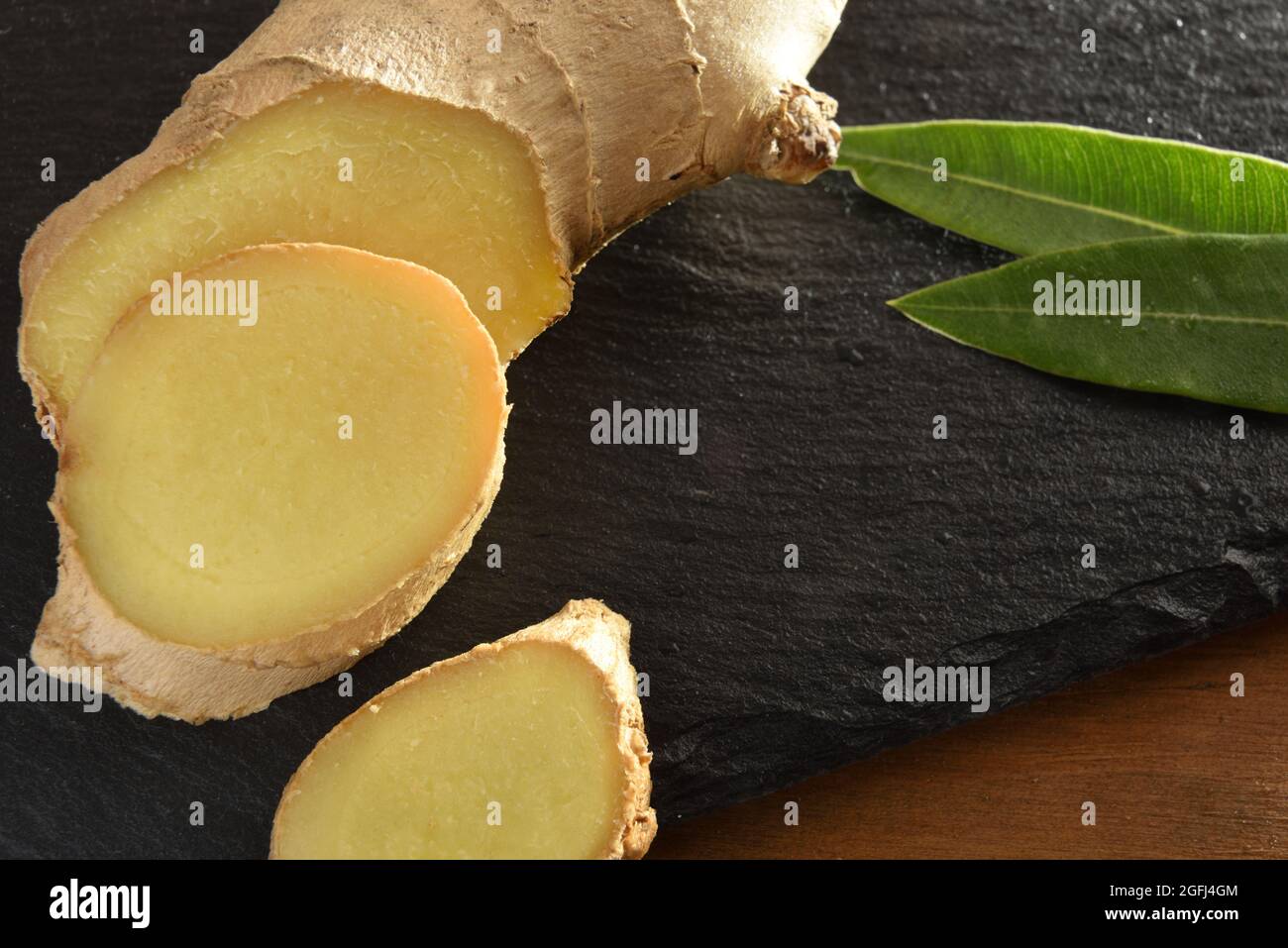 Ginger root slice on wooden cutting board on wooden table with leaves close up. Top view. Stock Photo