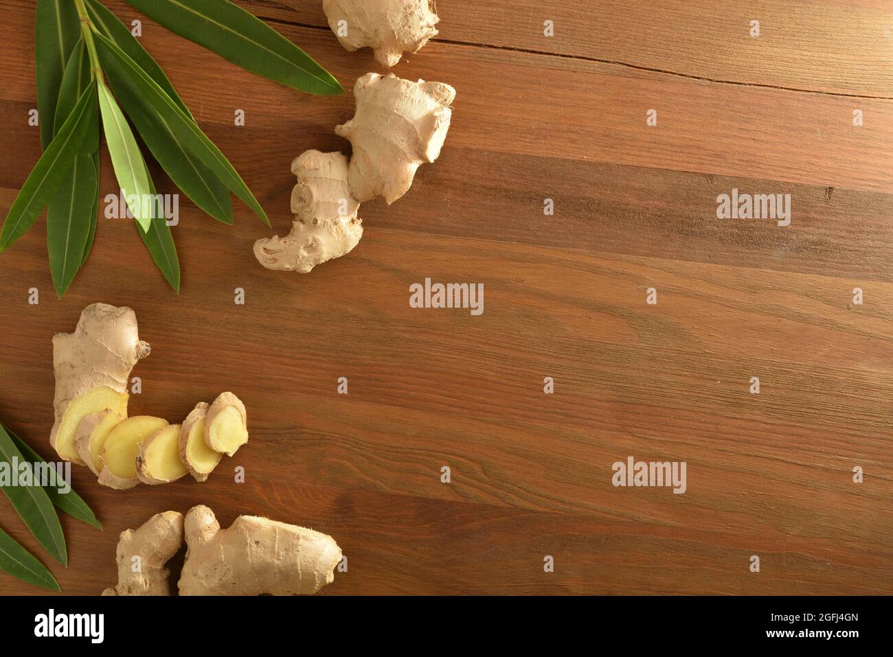 Ginger root as a product for healing purposes with sliced portions and leaves on wooden table. Top view. Stock Photo