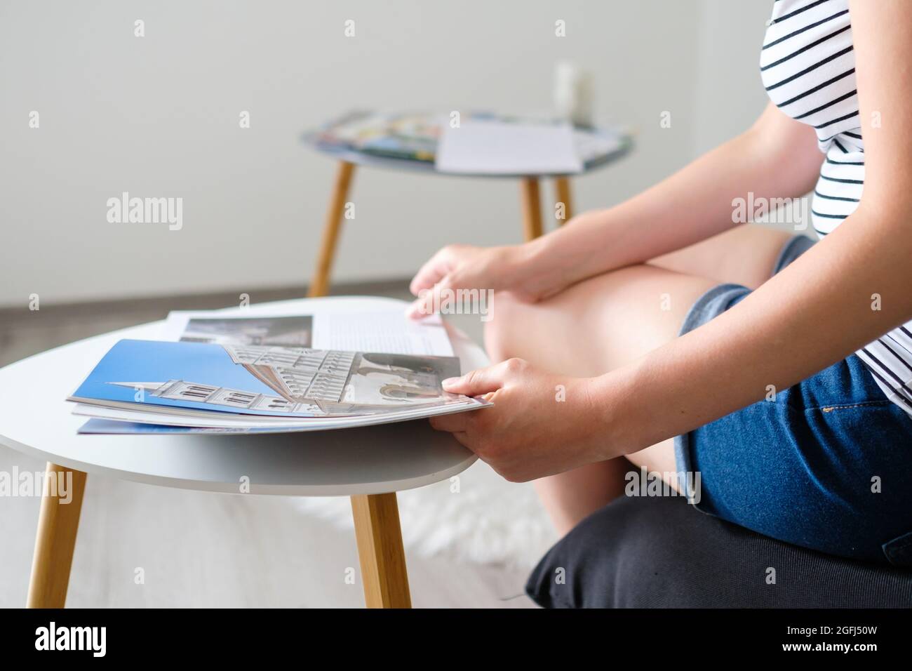 Young woman reading a catalog or travel magazine and chooses a destination to the trip in a beautiful modern living room Stock Photo
