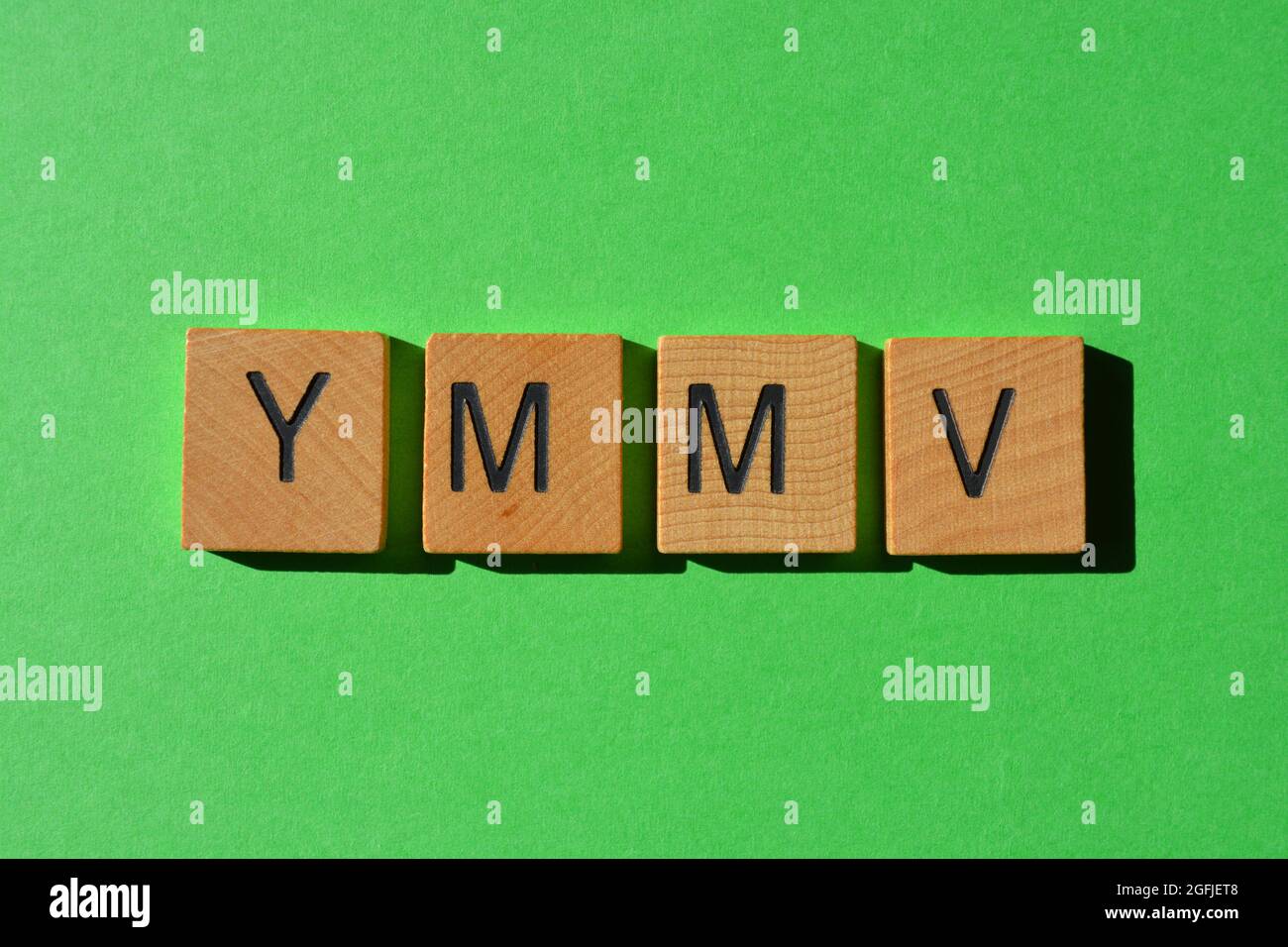 YMMV, Acronym for Your Mileage May Vary, in wooden alphabet letters isolated on green background Stock Photo