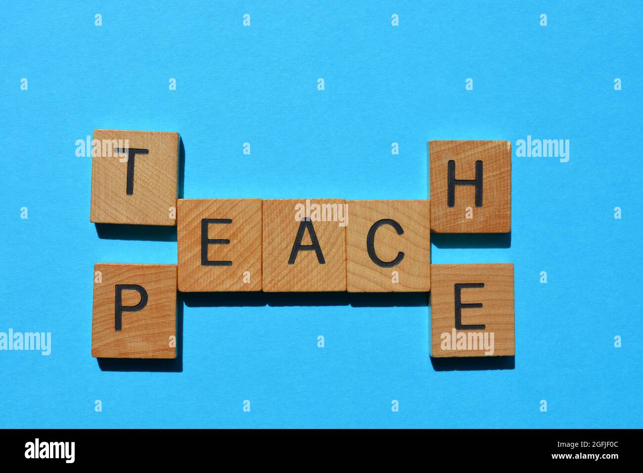Teach Peace, words in wooden alphabet letters isolated on blue background Stock Photo