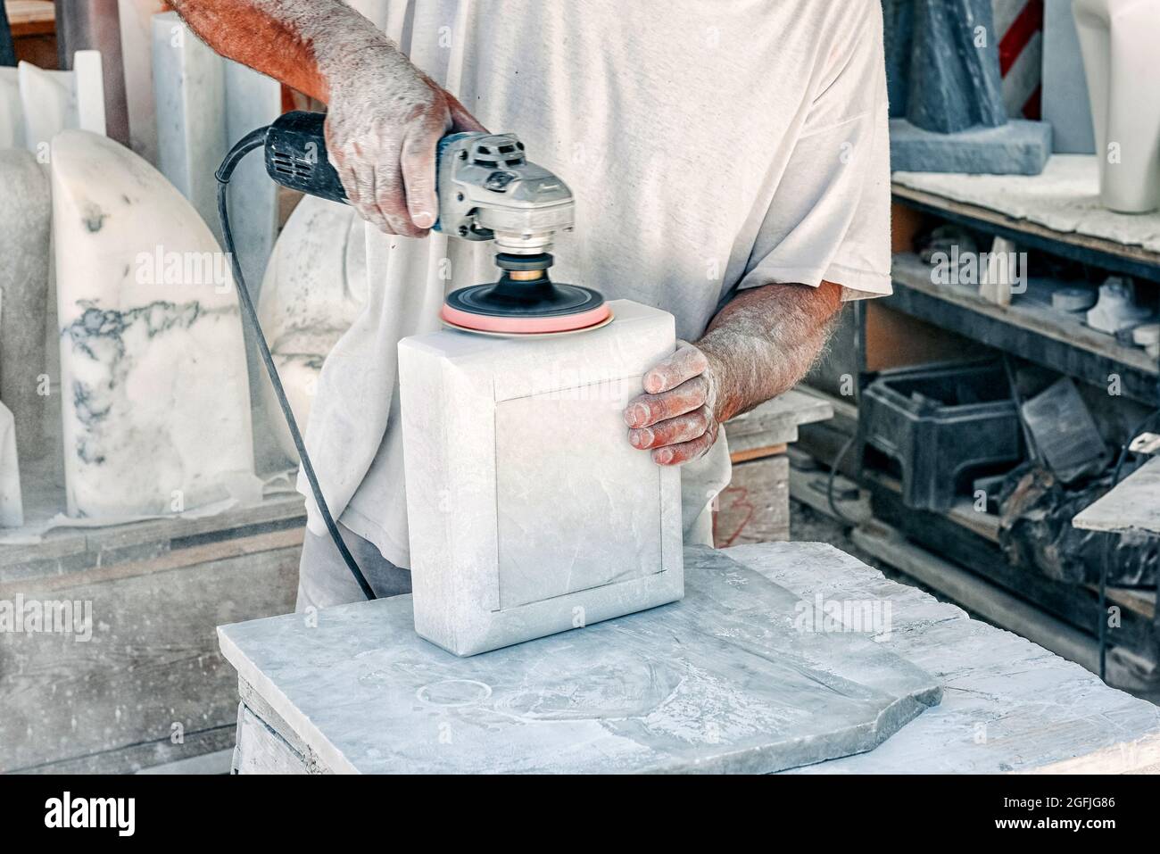 Man using an orbital sander to smooth a block of marble in a workshop during the production process in a close up on his hands and the power tool Stock Photo