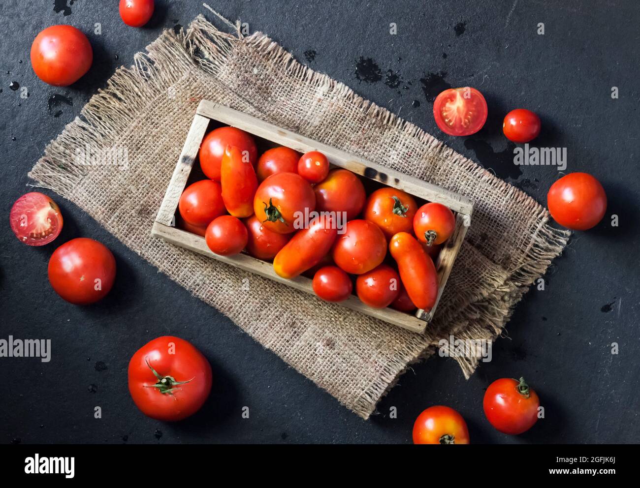 Fresh red tomatoes in wooden box on black background. Flat lay, top view Stock Photo