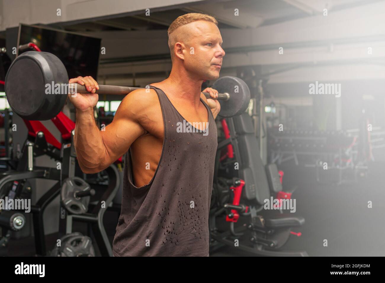 Confident muscular man training squats with barbells over head. Closeup portrait of professional bodybuilder flexing muscles with barbell in gym.Side Stock Photo