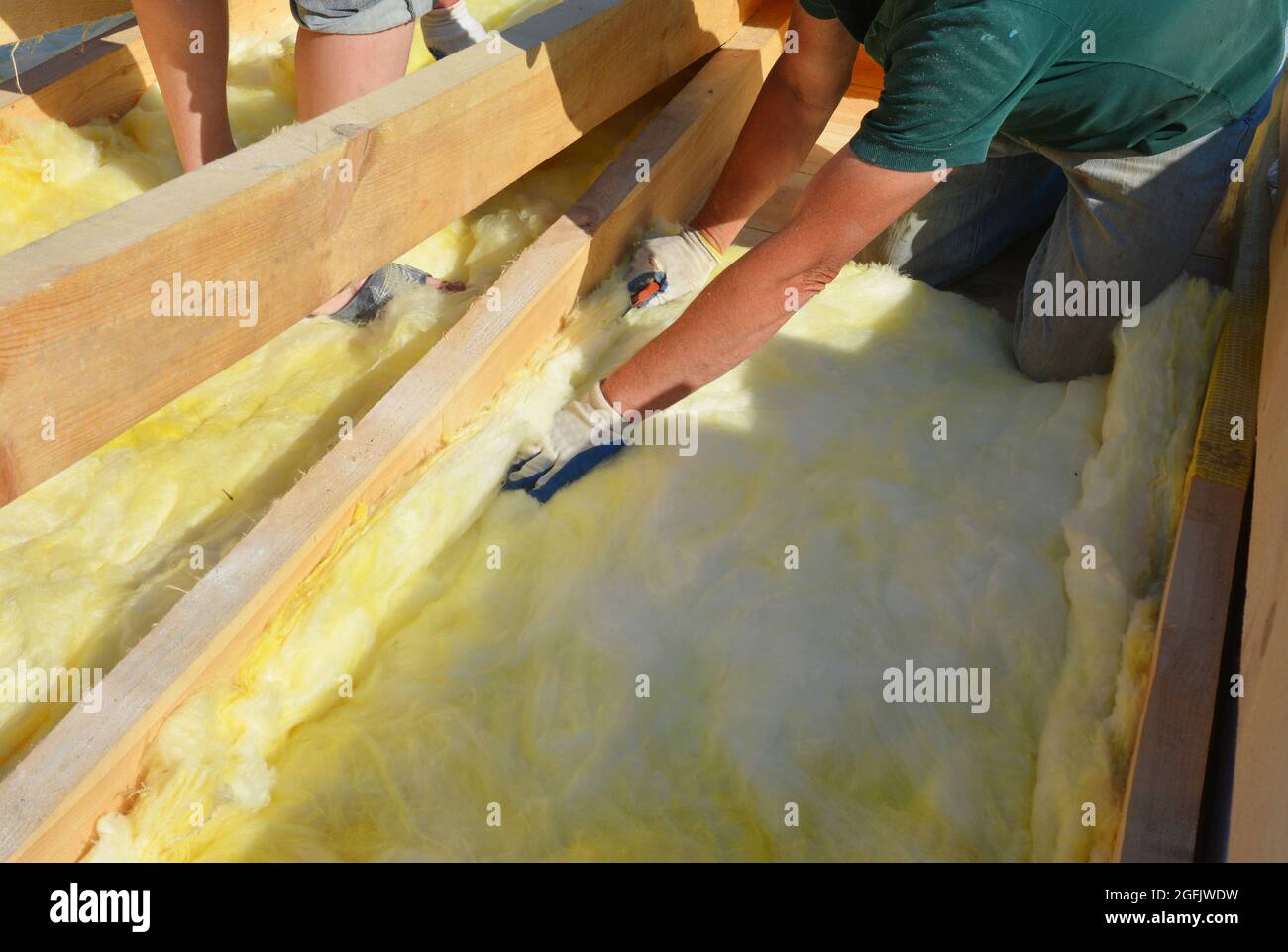 Roofing construction: building contractors in protective gloves are installing glass wool sheets, batts on the rooftop below trusses for thermal insul Stock Photo