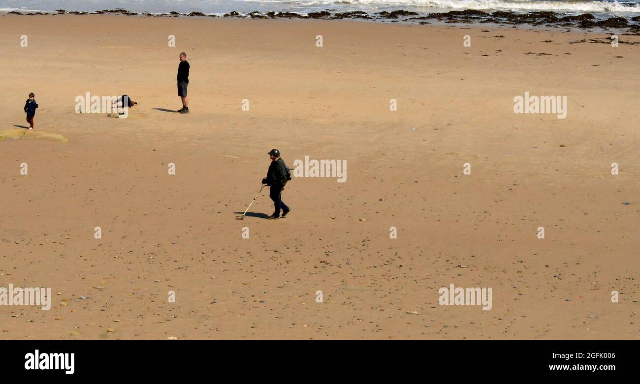 WHITLEY BAY. TYNE and WEAR. ENGLAND. 05-27-21. The beach with a man using a metal detector. There is also a family group. The tide is beginning to com Stock Photo