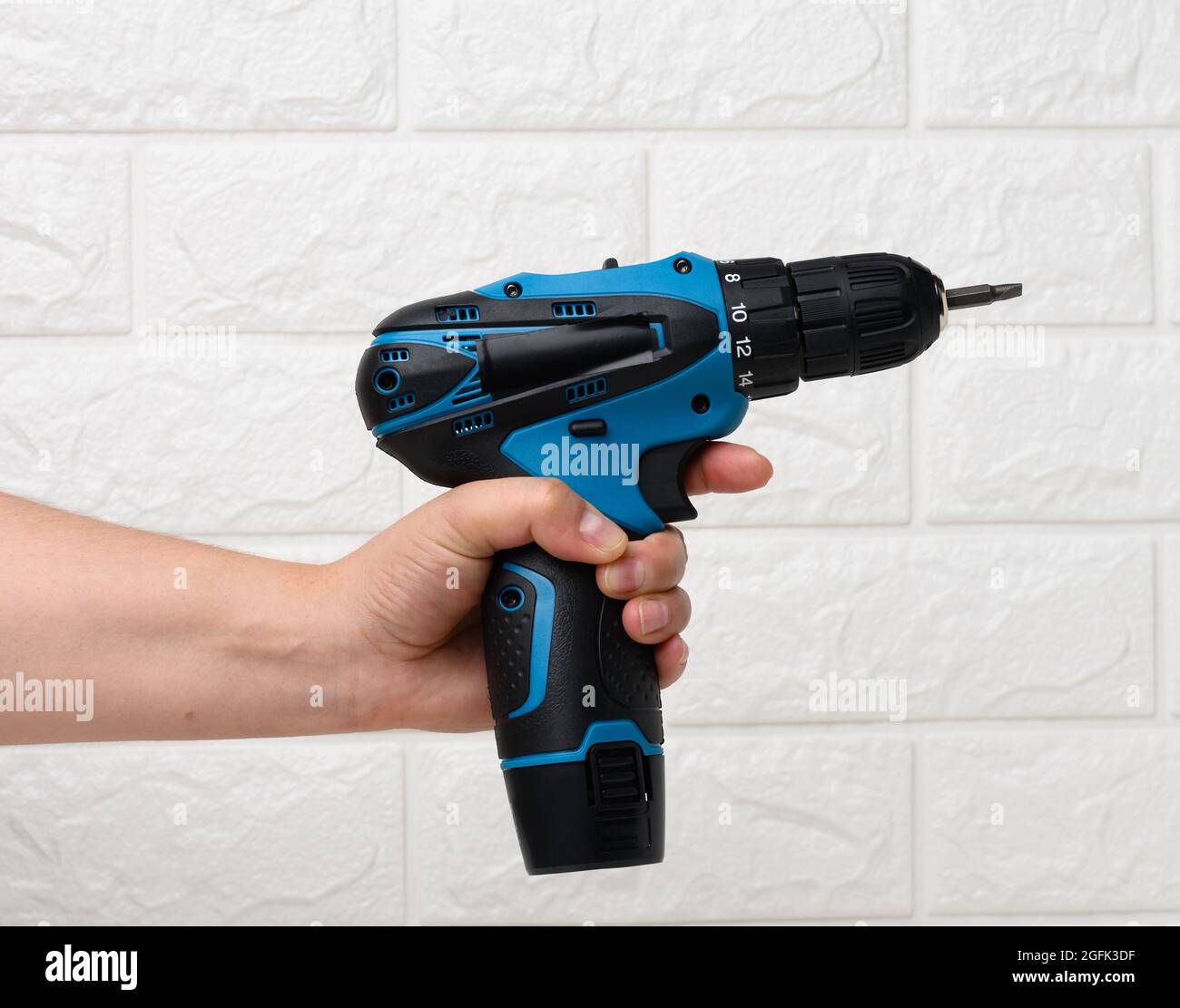 https://c8.alamy.com/comp/2GFK3DF/hand-in-a-textile-glove-holds-a-portable-drill-on-a-battery-against-a-background-of-a-white-brick-wall-2GFK3DF.jpg