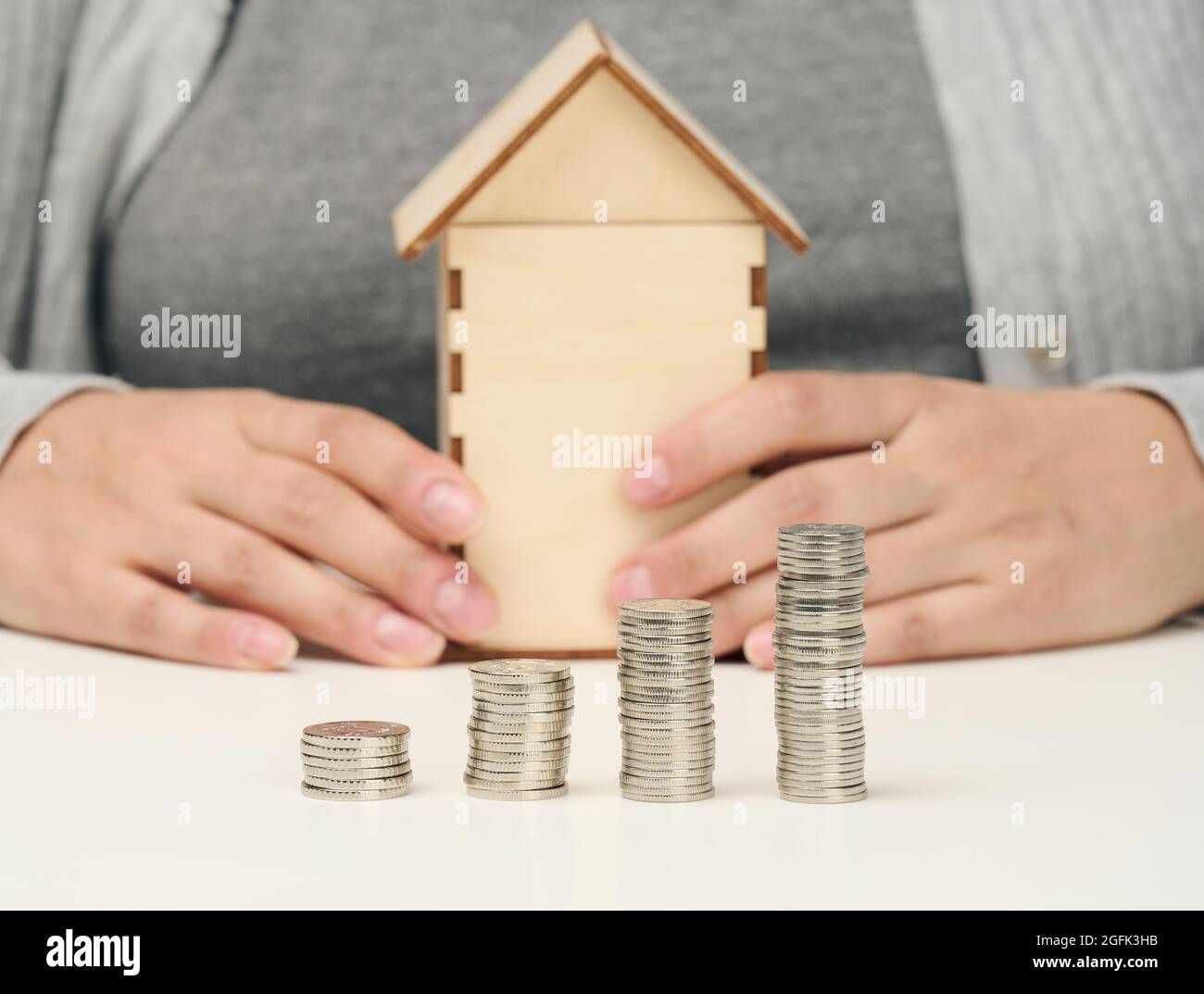 wooden model of a house, a stack of coins. The man sits at the table. Higher property prices, higher rents and higher mortgage interest rates Stock Photo