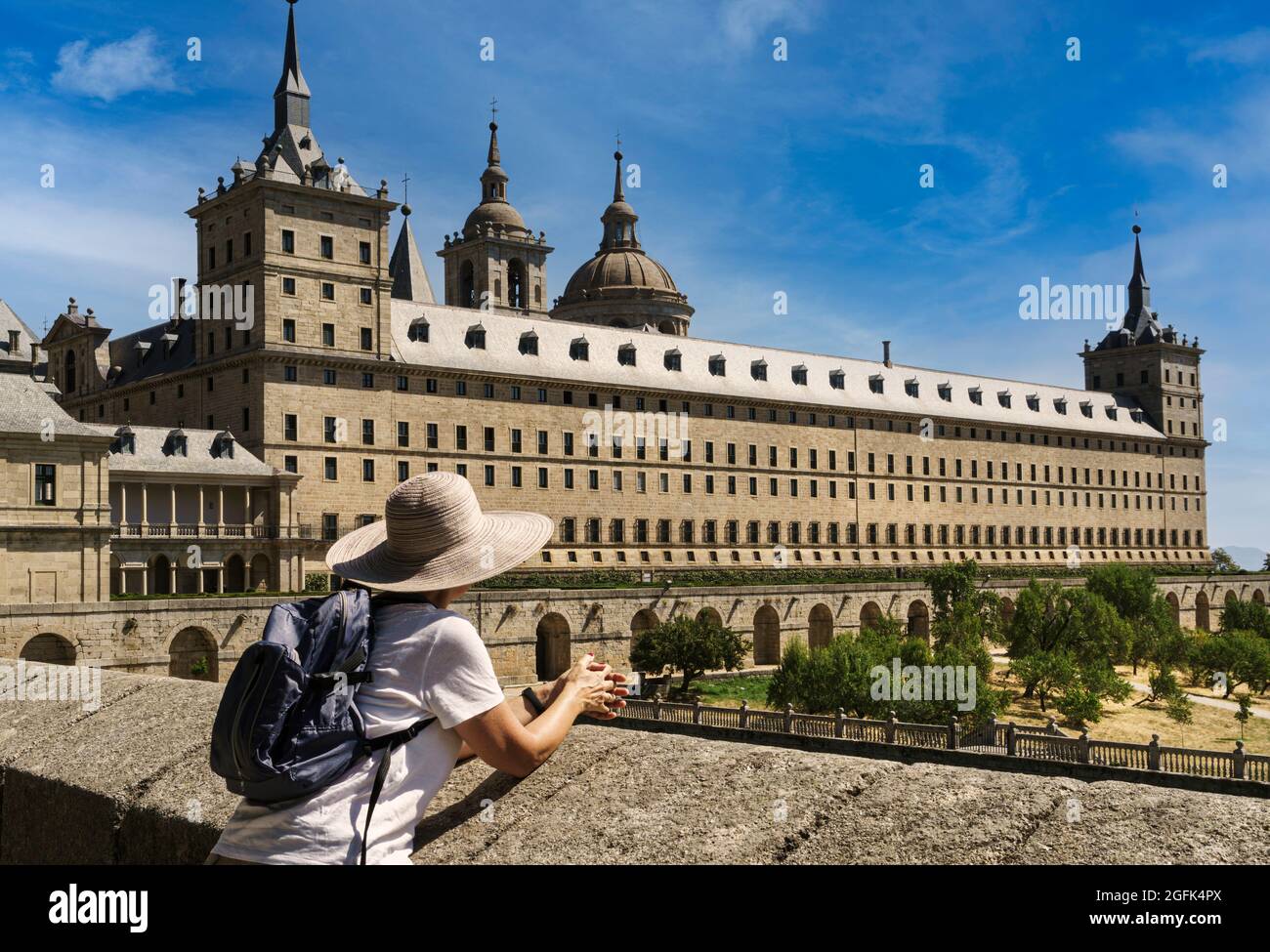 Mature woman with hat and small backpack contemplating the monument of the monastery of San Lorenzo de El Escorial, in summer and with blue sky and li Stock Photo