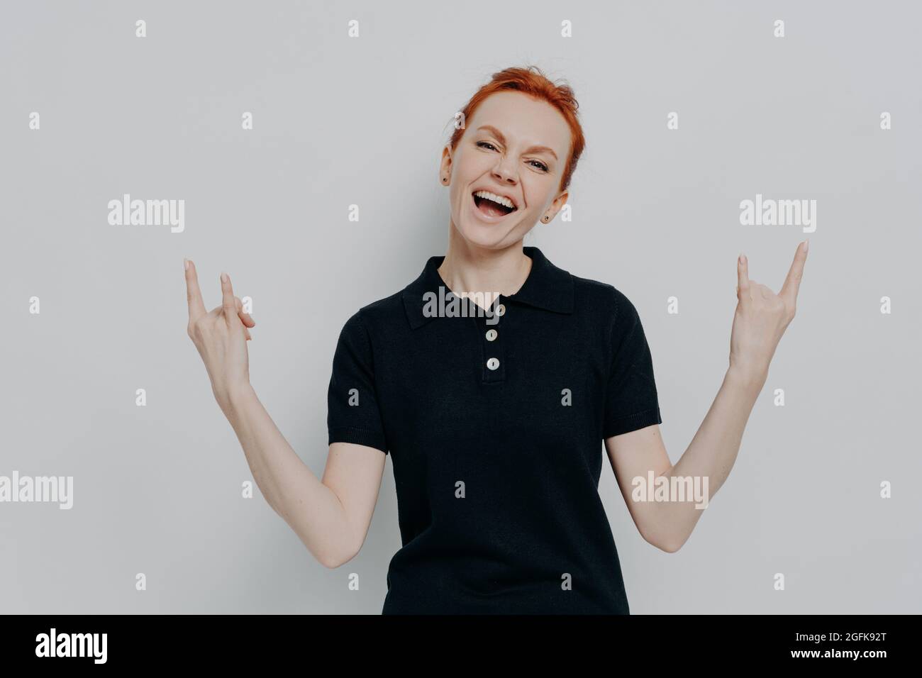Energetic crazy young woman with red hair holding hands in rock and roll sign and screaming Stock Photo