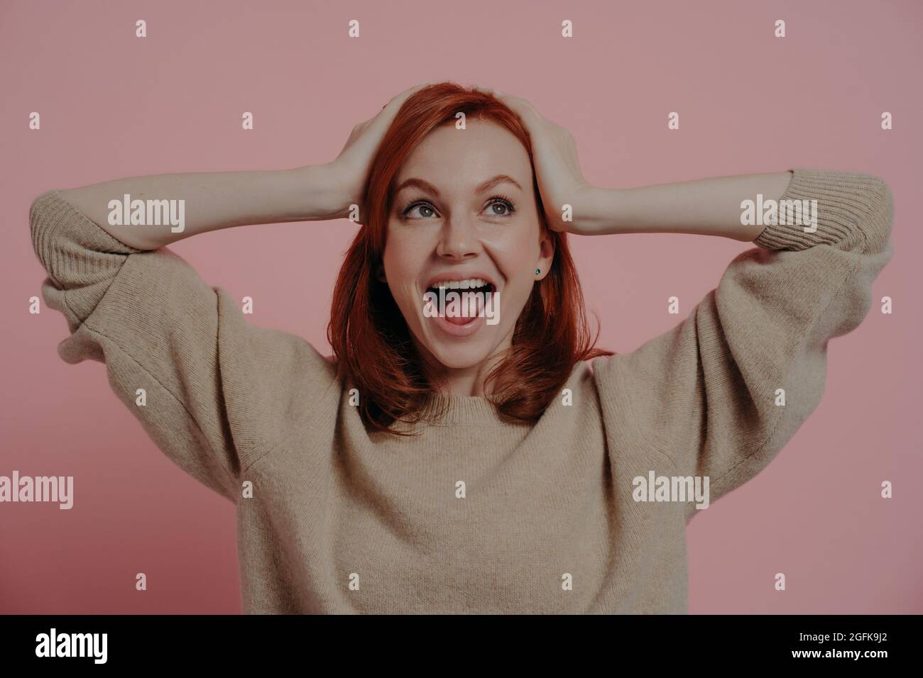 Surprised shocked european female holding head in hands and looking upside with excited expression Stock Photo