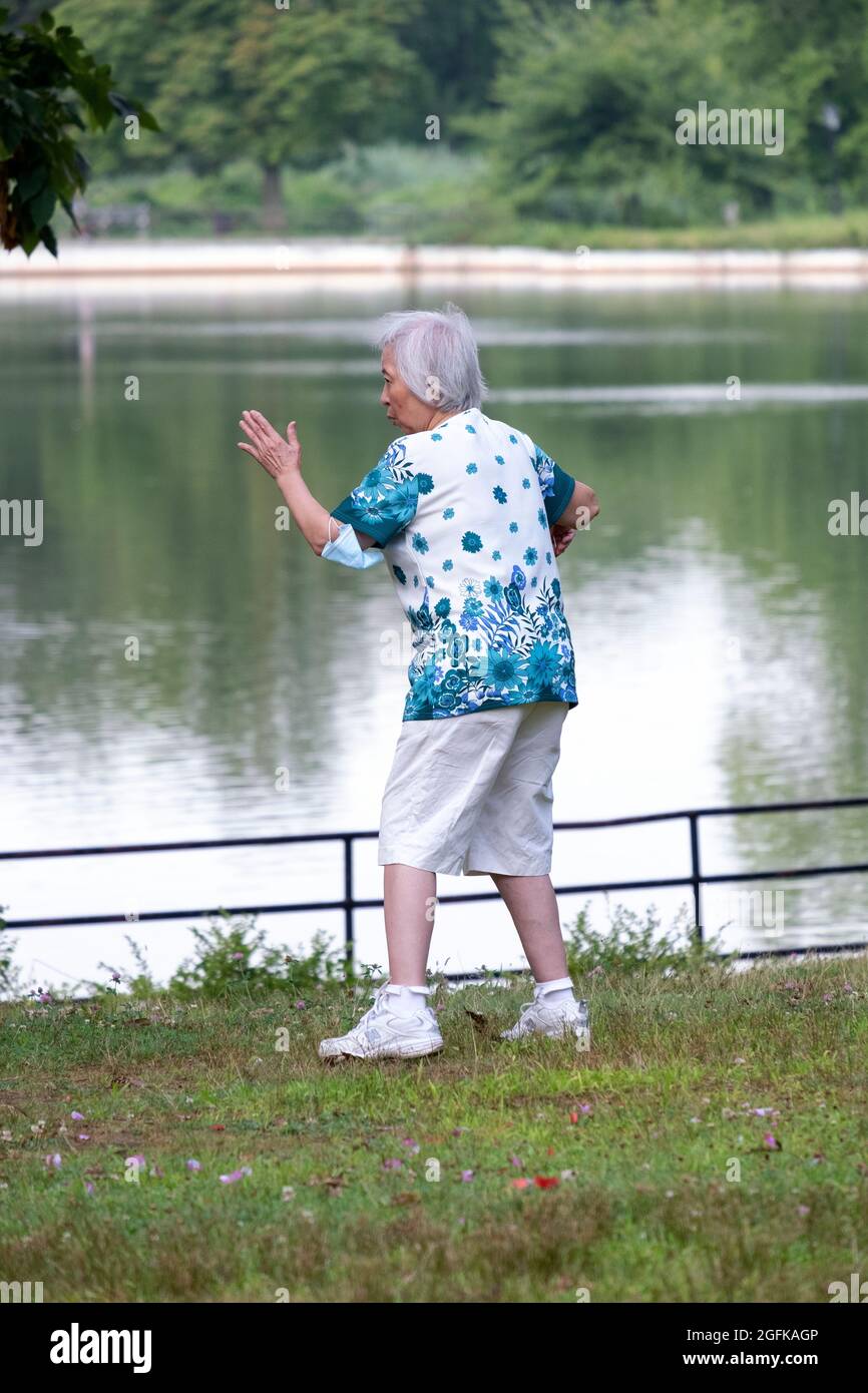 An older woman, likely in her 70's, goes through graceful Thai Chi motions in a park in Queens, New York City. Stock Photo