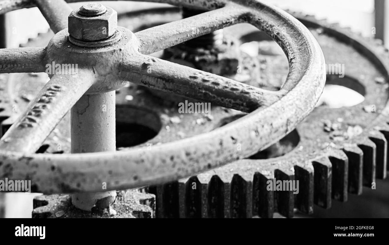 Old grunge steampunk valve wheel with gear gearbox selective focus with handle grip over out of focus industrial metal BW background 16x9 with Stock Photo