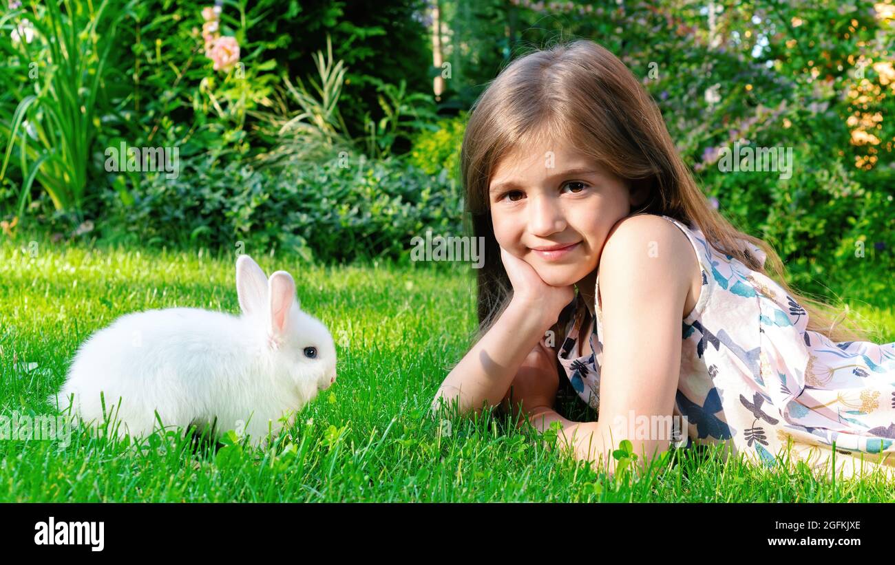A beautiful girl lies on the lawn and plays with a baby bunny