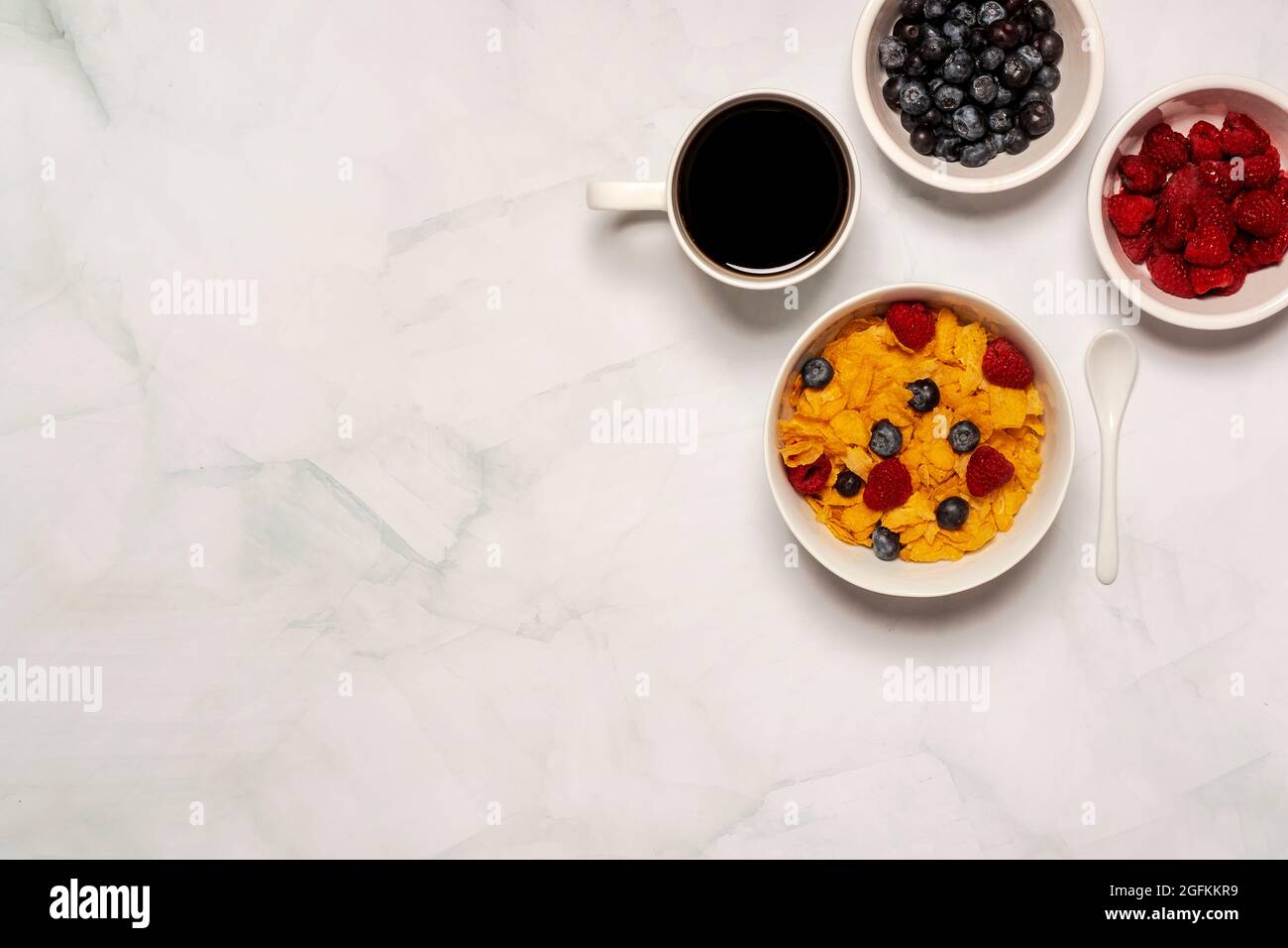 Working morning breakfast of cornflakes cereal with raspberries and blueberries with black coffee and a bagel with cream cheese Stock Photo