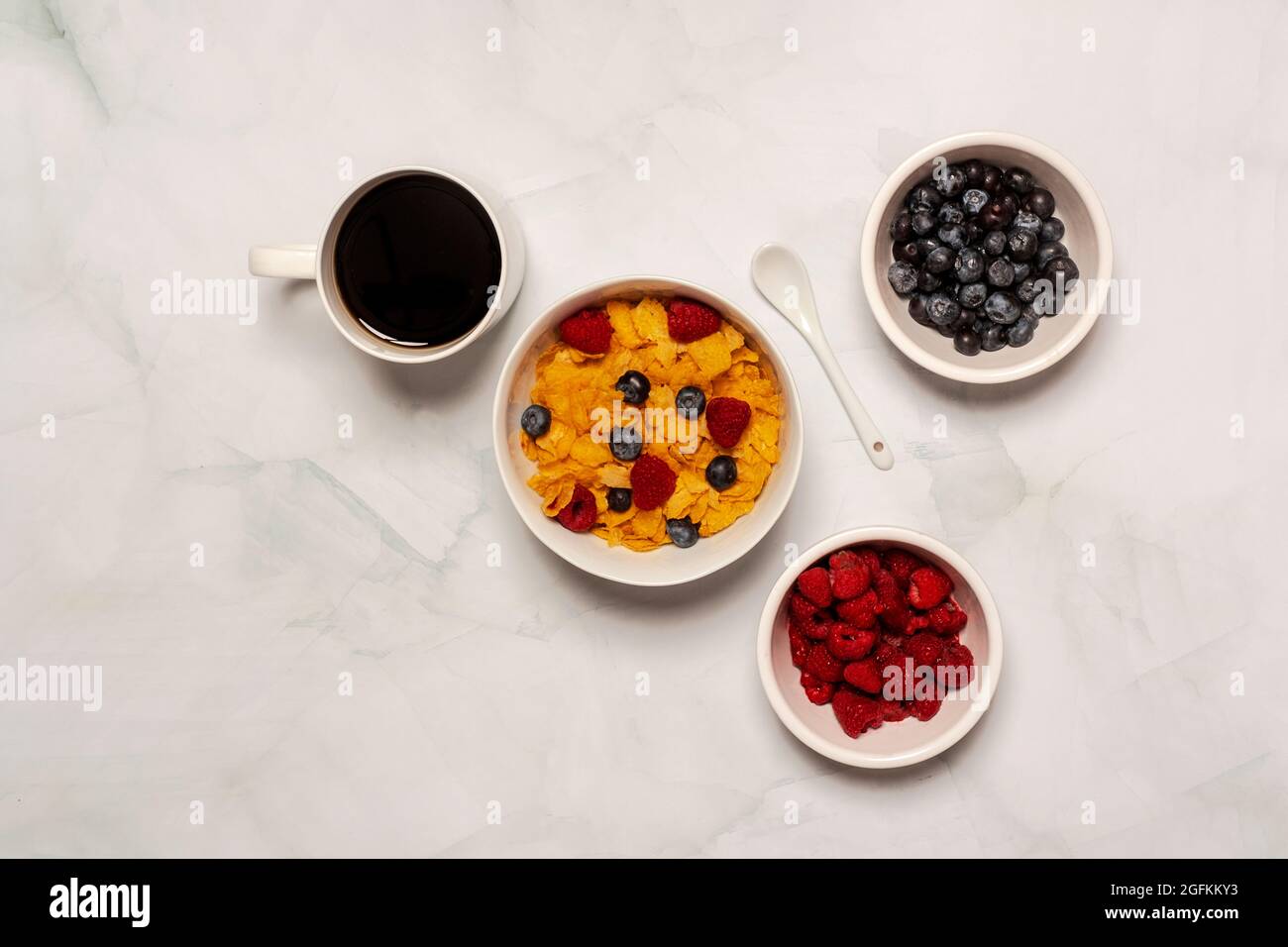 Morning breakfast consisting of cornflake cereal with fresh raspberries and blueberries with black coffee Stock Photo