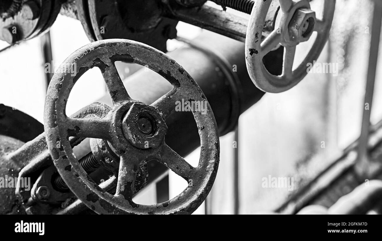 Two old grunge steampunk valve wheels selective focus with handle grip over out of focus industrial metal BW background 16x9 with copyspace in black Stock Photo