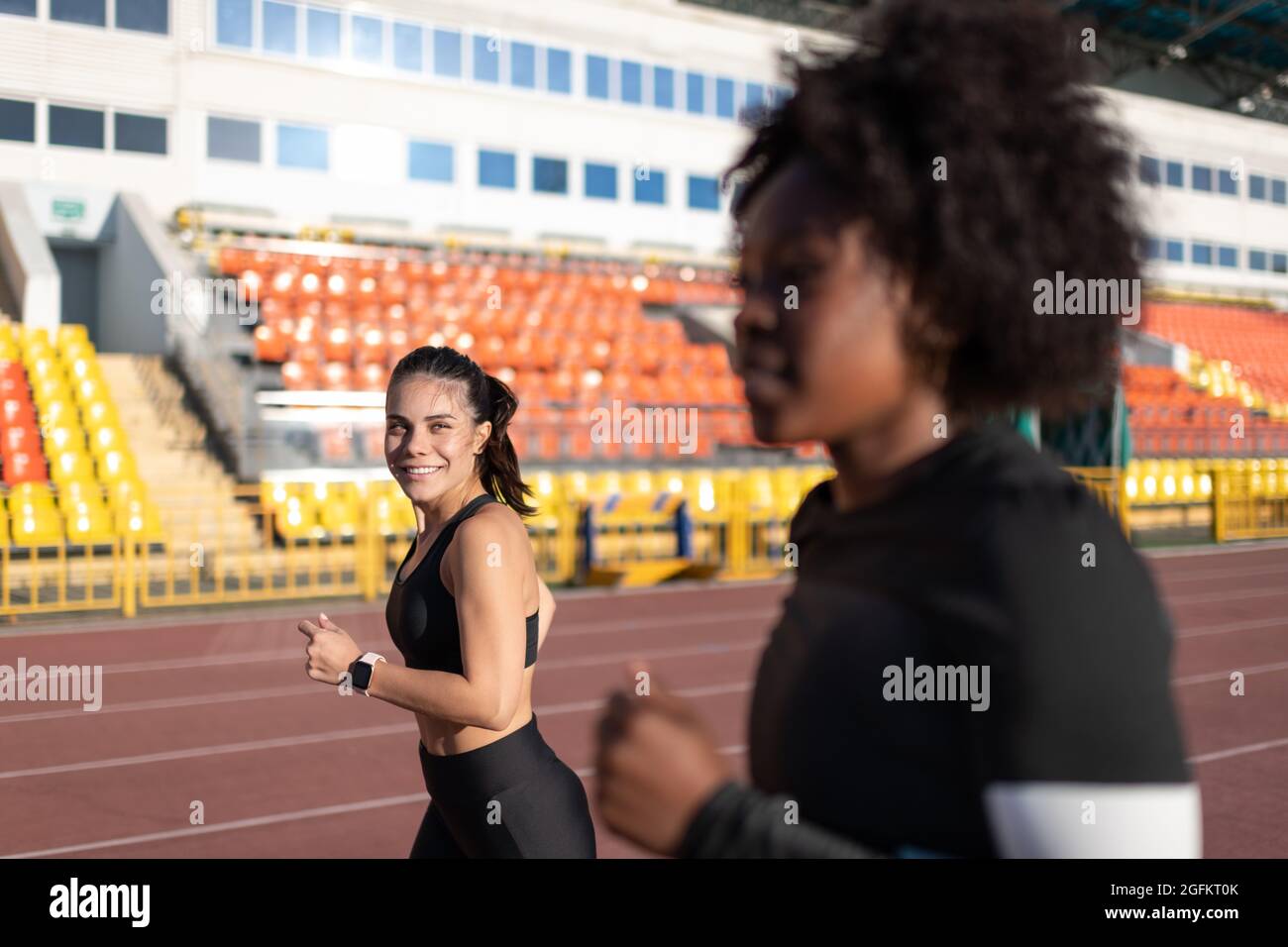 Positive athlete looking at black girlfriend while running on track together Stock Photo