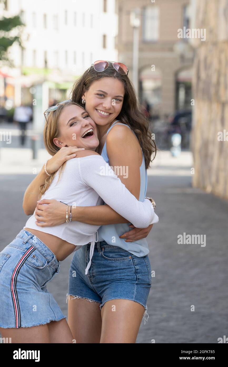 two young women hugging and laughing in street of a city Stock Photo