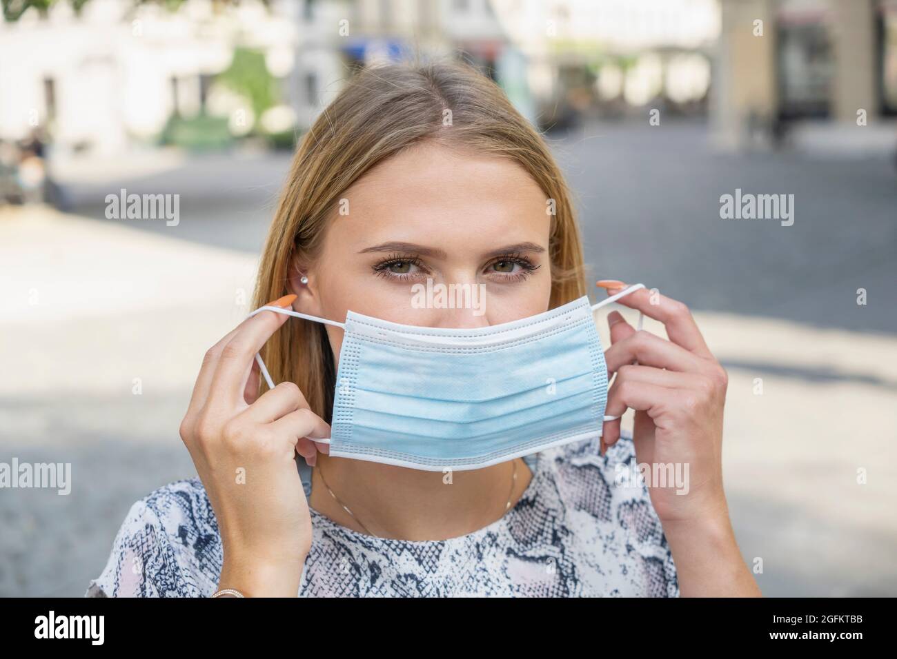 Young woman put on a protective mask because of Covid outdoor in City Stock Photo