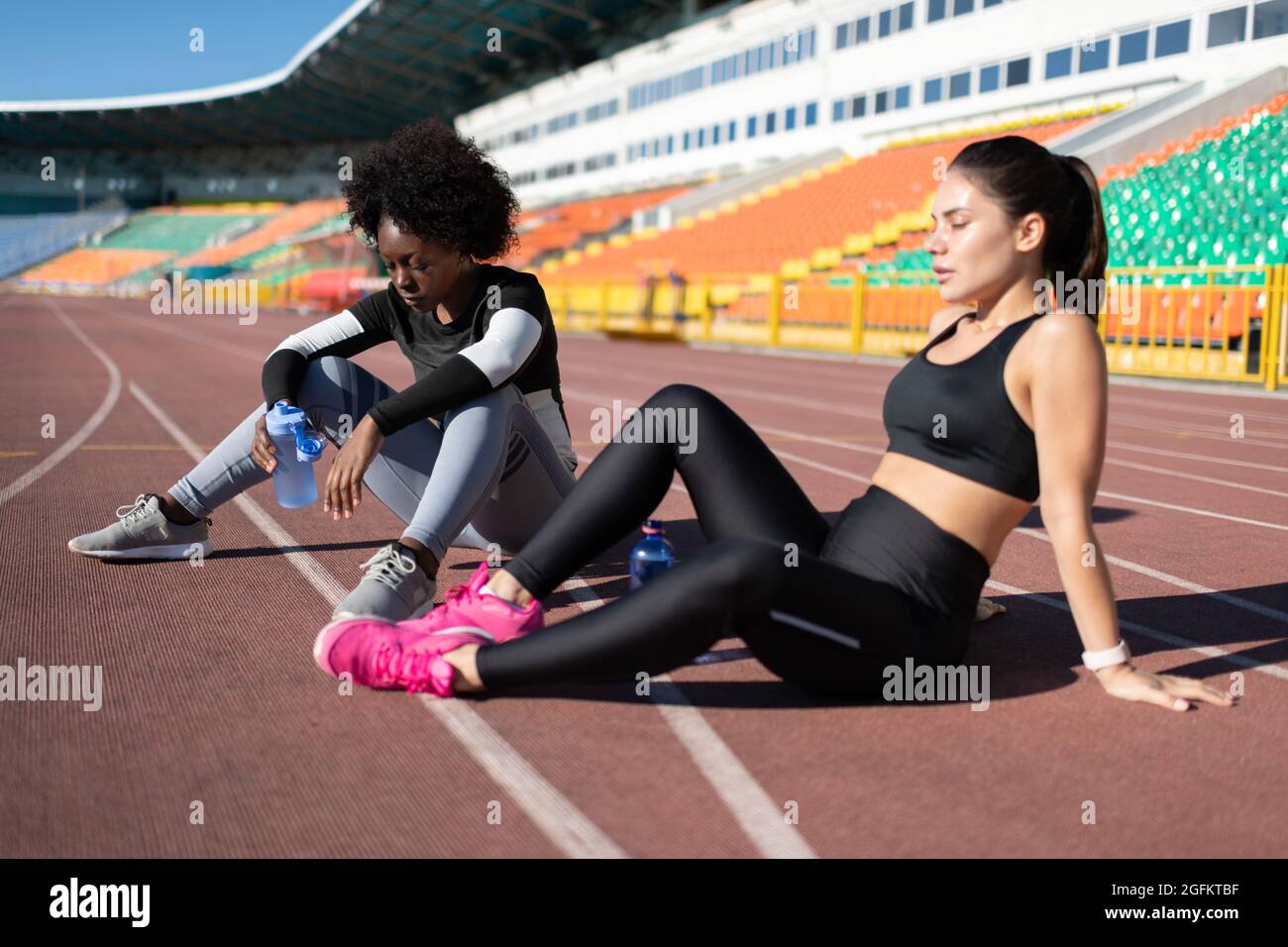 Diverse exhausted runners sitting on track and resting during break on stadium Stock Photo