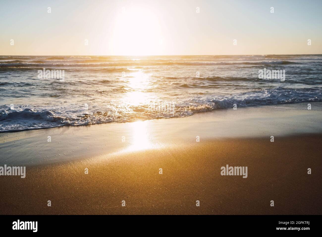 waves breaking on the shore of the beach with foam at sunset Stock Photo