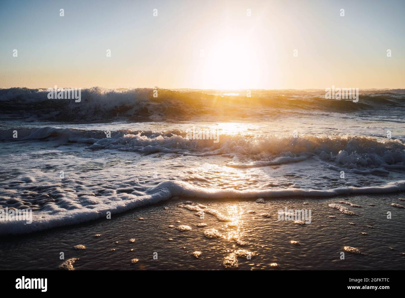 waves breaking on the shore of the beach with foam at sunset Stock Photo