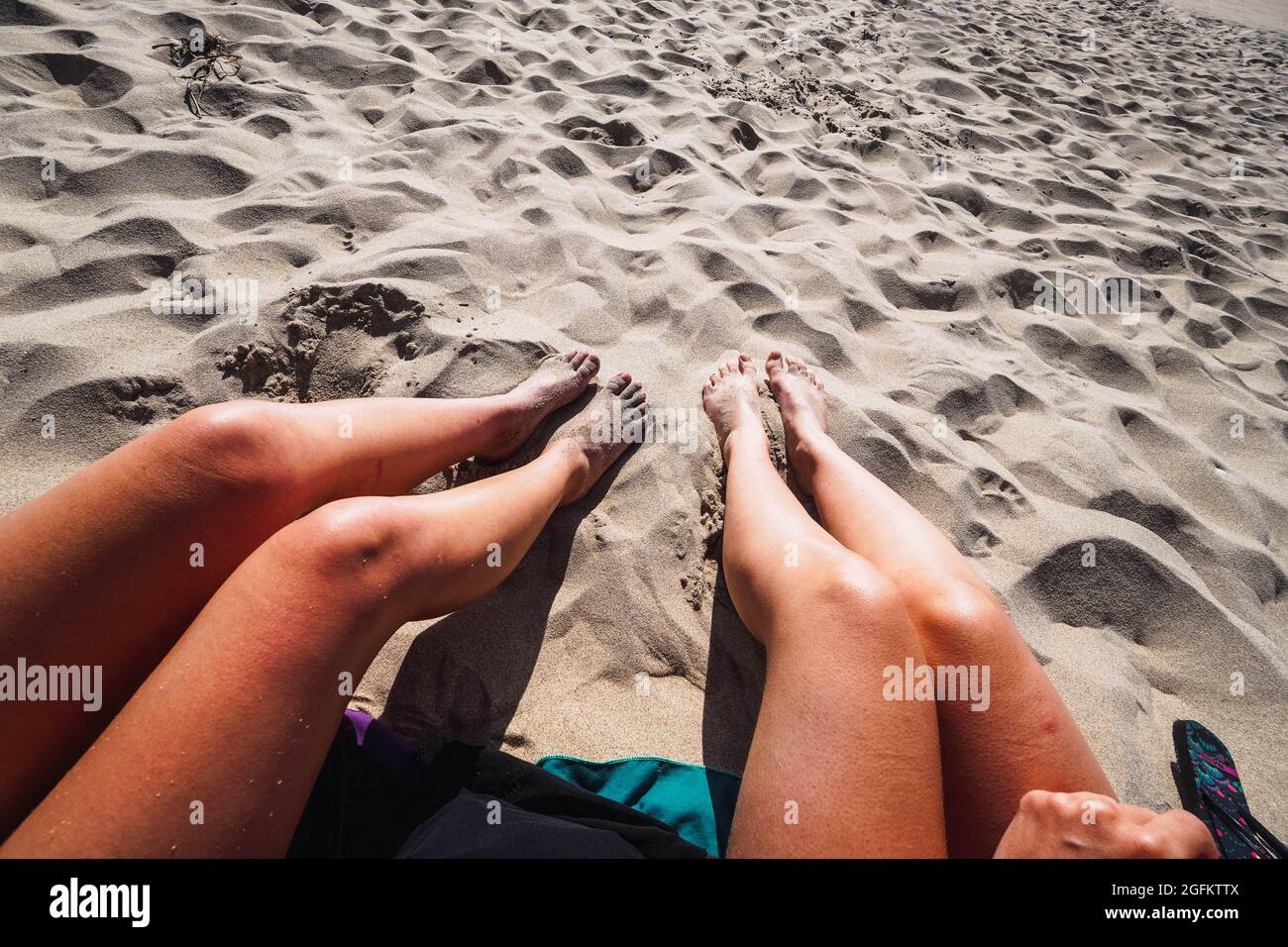 two pair of women's legs in the sand on the beach Stock Photo