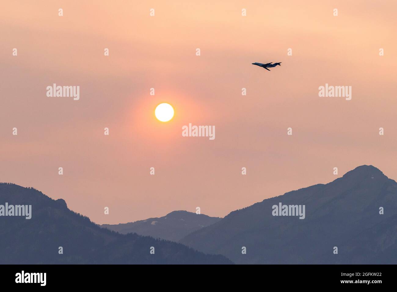 California wildfire smoke and a jet at dusk in Jackson, WY. Stock Photo