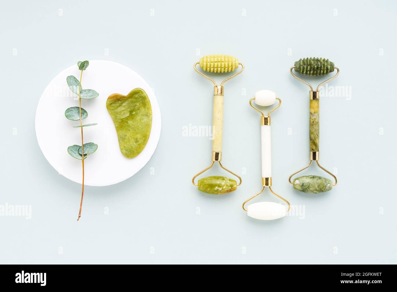 Massage tools. Guasha massager, jade facial rollers and eucalyptus branches on a gray background. SPA concept. Top view, copy space for text Stock Photo