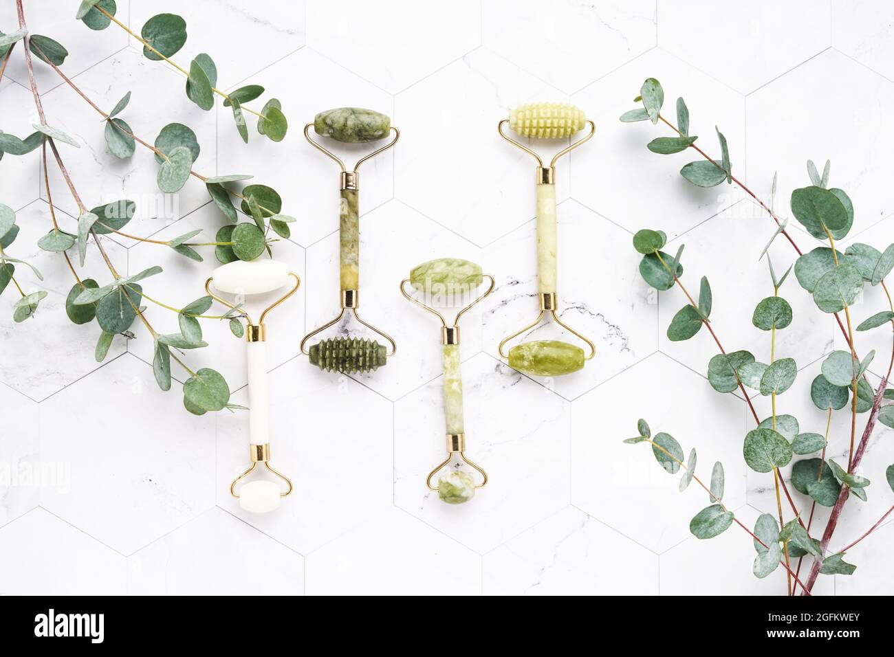 Jade face rollers and eucalyptus branches on a white marble background. SPA concept. Top view, copy space for text Stock Photo