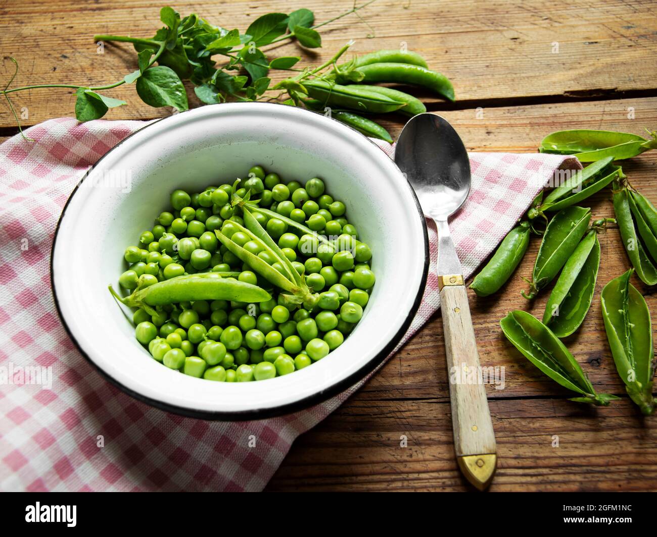 Fresh green peas in a white bowl, pods, on the table Stock Photo
