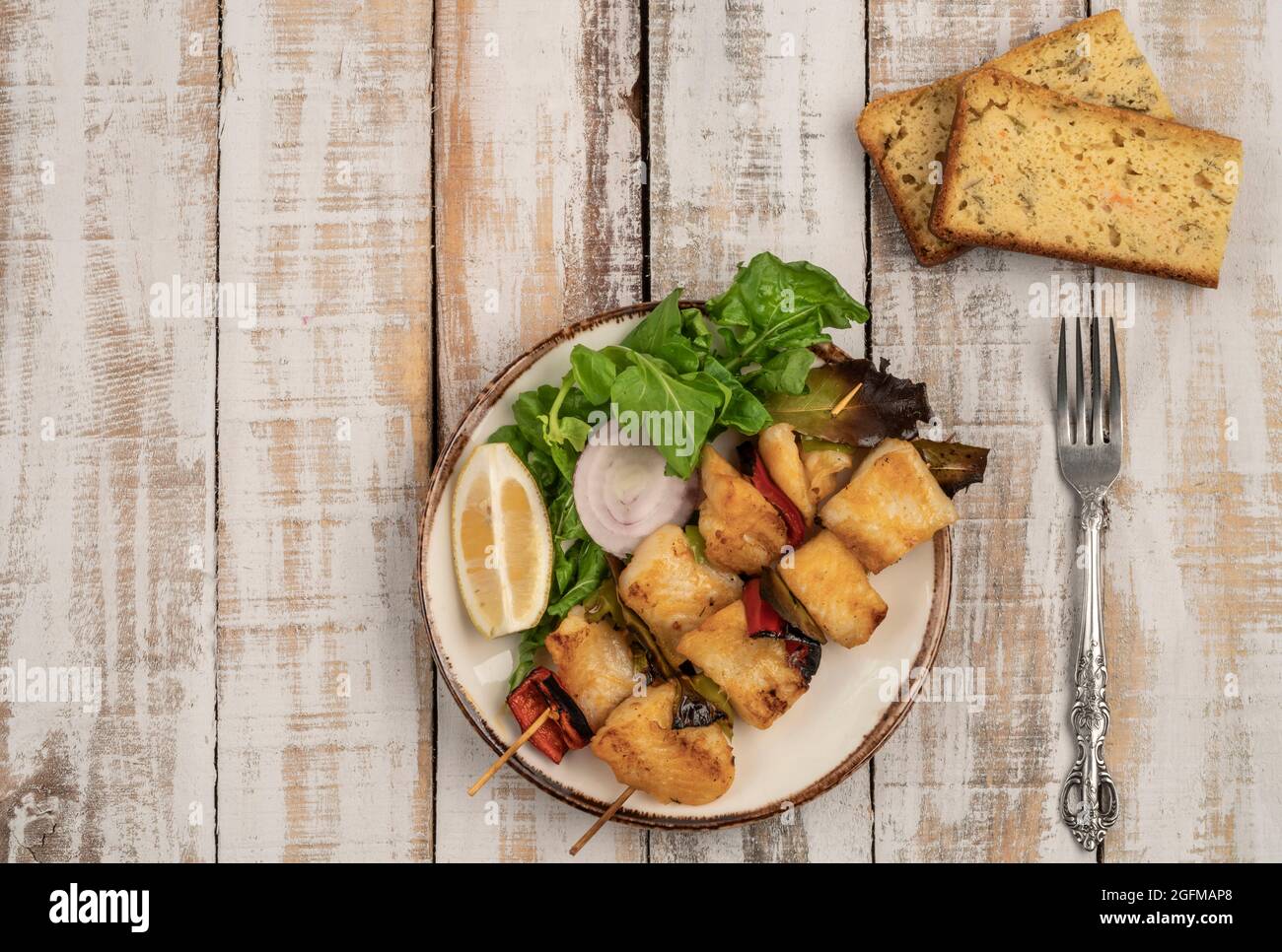 Skewed sole fish served with salad and corn bread on a wooden table Stock Photo