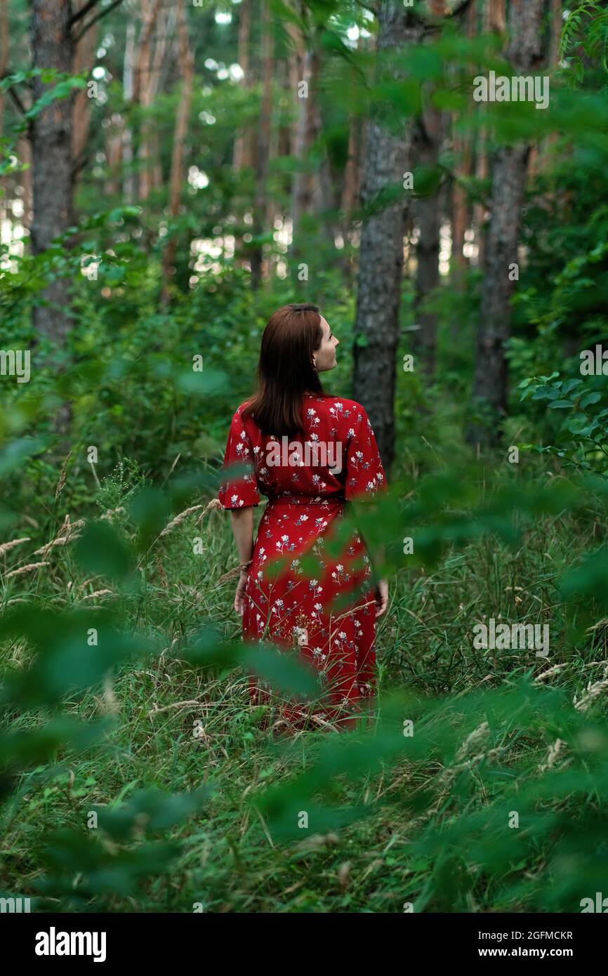 JOMO, joy of missing out, Connecting with nature, mental healing, mental health, calmness concept. Young woman in red dress and straw hat walks alone Stock Photo