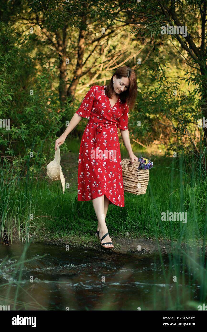 JOMO, joy of missing out, Connecting with nature, mental healing, mental health, calmness concept. Young woman in red dress and straw hat walks alone Stock Photo