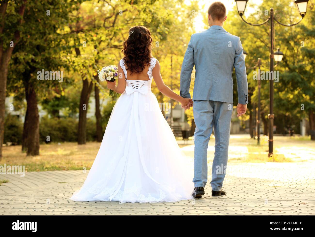 Beautiful young wedding couple holding hands while walking in park ...
