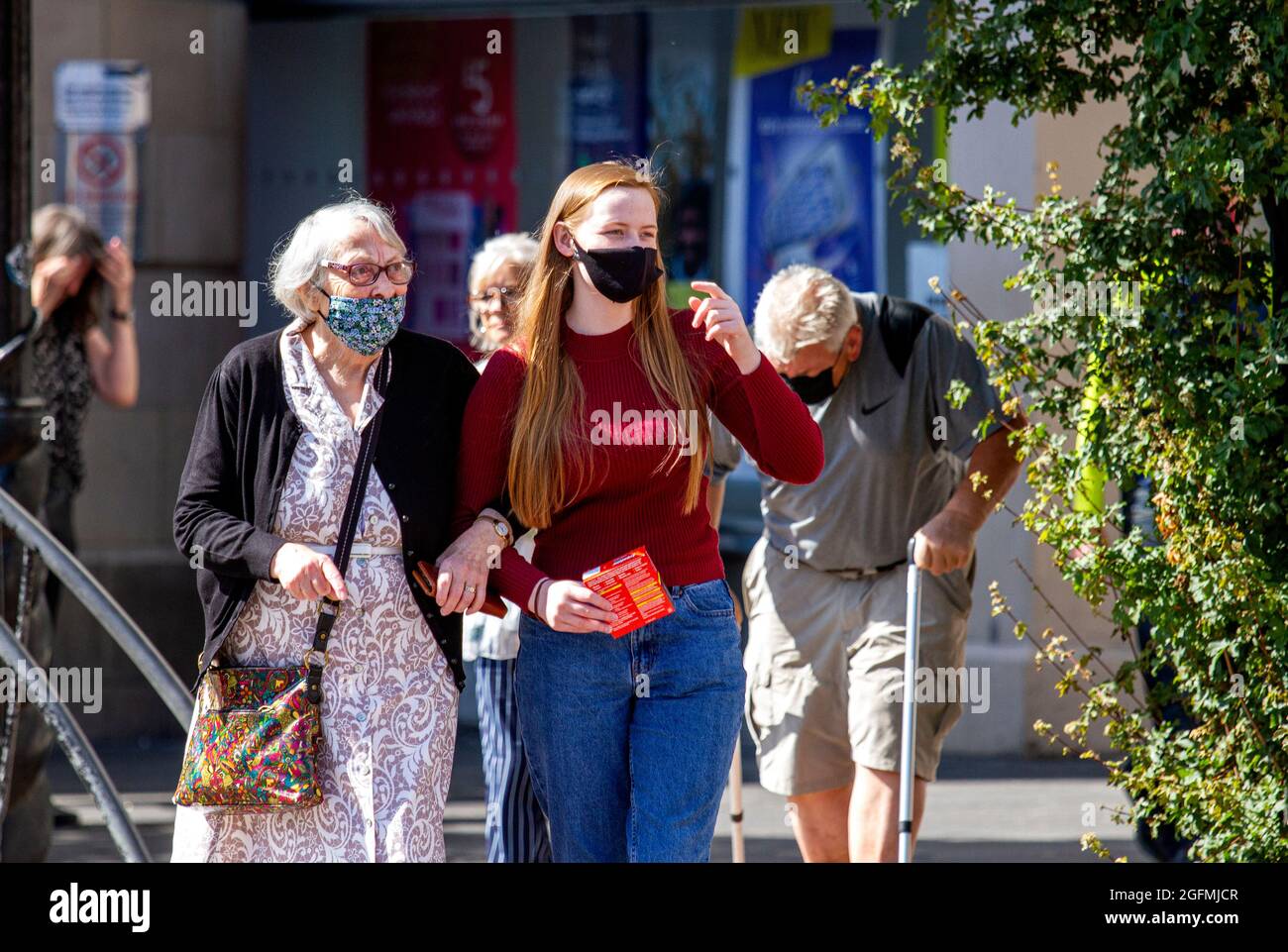 Dundee, Tayside, Scotland, UK. 26th Aug, 2021. UK Weather: A warm sunny day with a slight cool breeze across North East Scotland with temperatures reaching 20°C. A young woman with her grandmother wearing facemasks walking arm in arm in the warm sunshine whilst enjoying a day out in Dundee city centre. Credit: Dundee Photographics/Alamy Live News Stock Photo