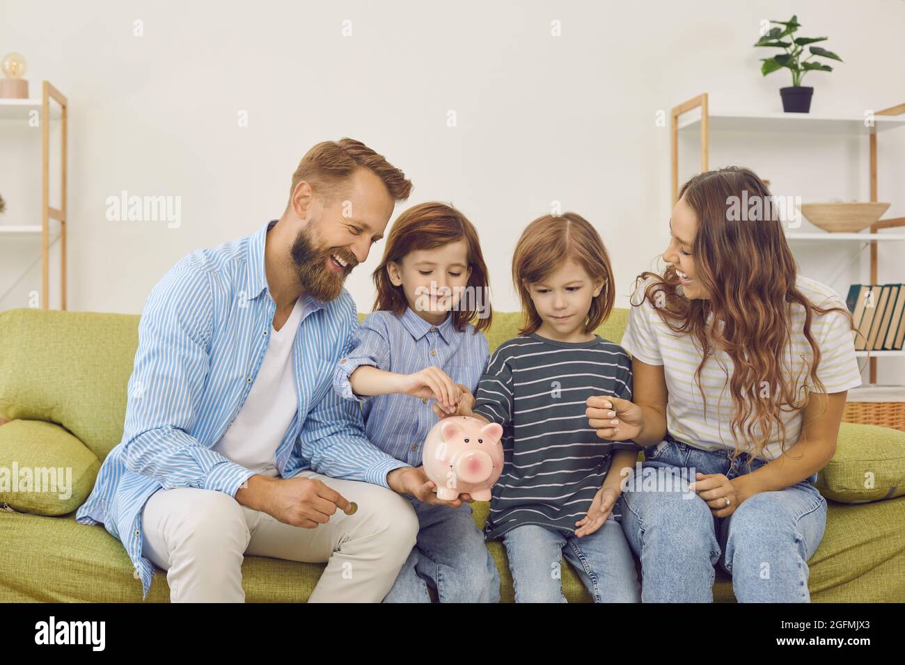Happy mother, father and children decide to save up and put coins inside piggy bank Stock Photo