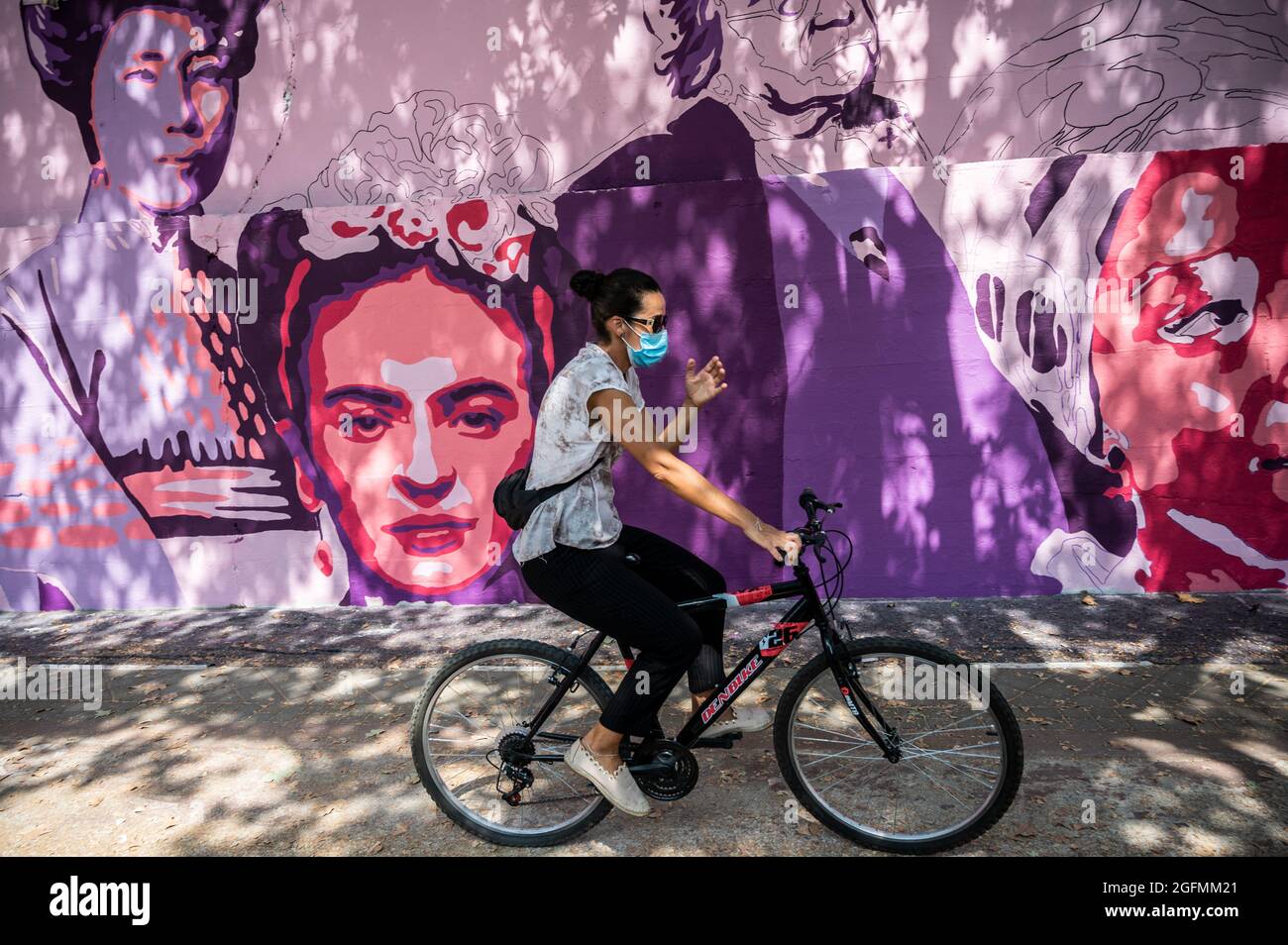 Madrid, Spain, 26/08/2021, A woman riding a bike passing by a feminist mural that is being repainted by members of UNLOGIC artistic group. The mural appeared vandalized during the past International Women's Day and represents famous women from around the world, with the faces of 15 women who are part of history for their fight in favor of equality: Angela Davis, Frida Kahlo, Nina Simone, Rigoberta Menchu, Lucia Sanchez Saornil, Rosa Arauzo, Valentina Tereshkova, Chimamanda Ngozi, Emma Goldman, Kanno Sugato, Liudmila Pavlichenko, Billy Jean King, Gata Cattana, Rosa Parks, and Comandanta Ramona. Stock Photo