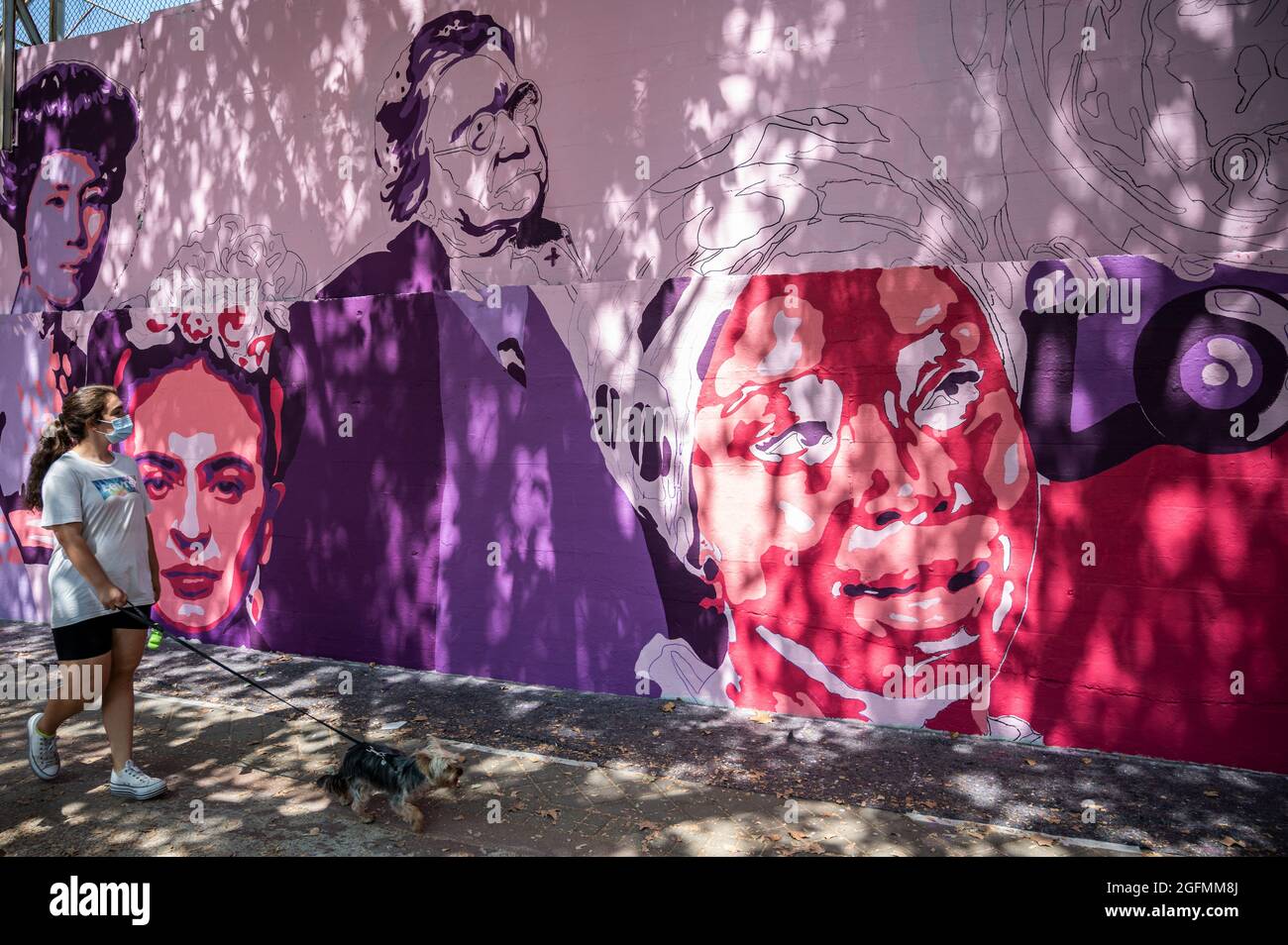 Madrid, Spain, 26/08/2021, A woman passing by a feminist mural that is being repainted by members of UNLOGIC artistic group. The mural appeared vandalized during the past International Women's Day and represents famous women from around the world, with the faces of 15 women who are part of history for their fight in favor of equality: Angela Davis, Frida Kahlo, Nina Simone, Rigoberta Menchu, Lucia Sanchez Saornil, Rosa Arauzo, Valentina Tereshkova, Chimamanda Ngozi, Emma Goldman, Kanno Sugato, Liudmila Pavlichenko, Billy Jean King, Gata Cattana, Rosa Parks, and Comandanta Ramona. Stock Photo