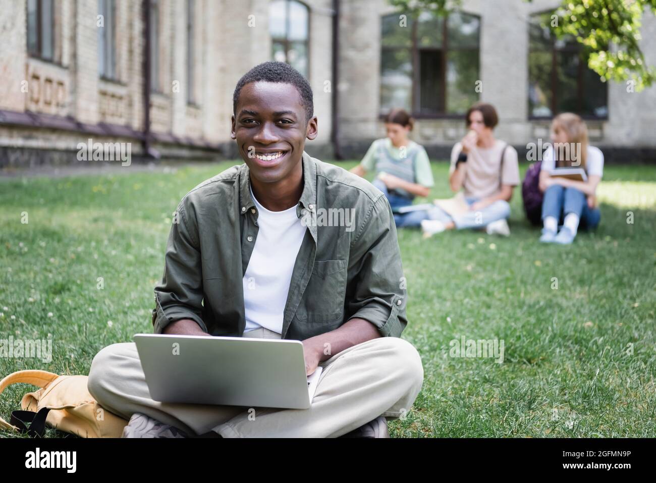 Cheerful african american student using laptop on lawn outdoors Stock ...