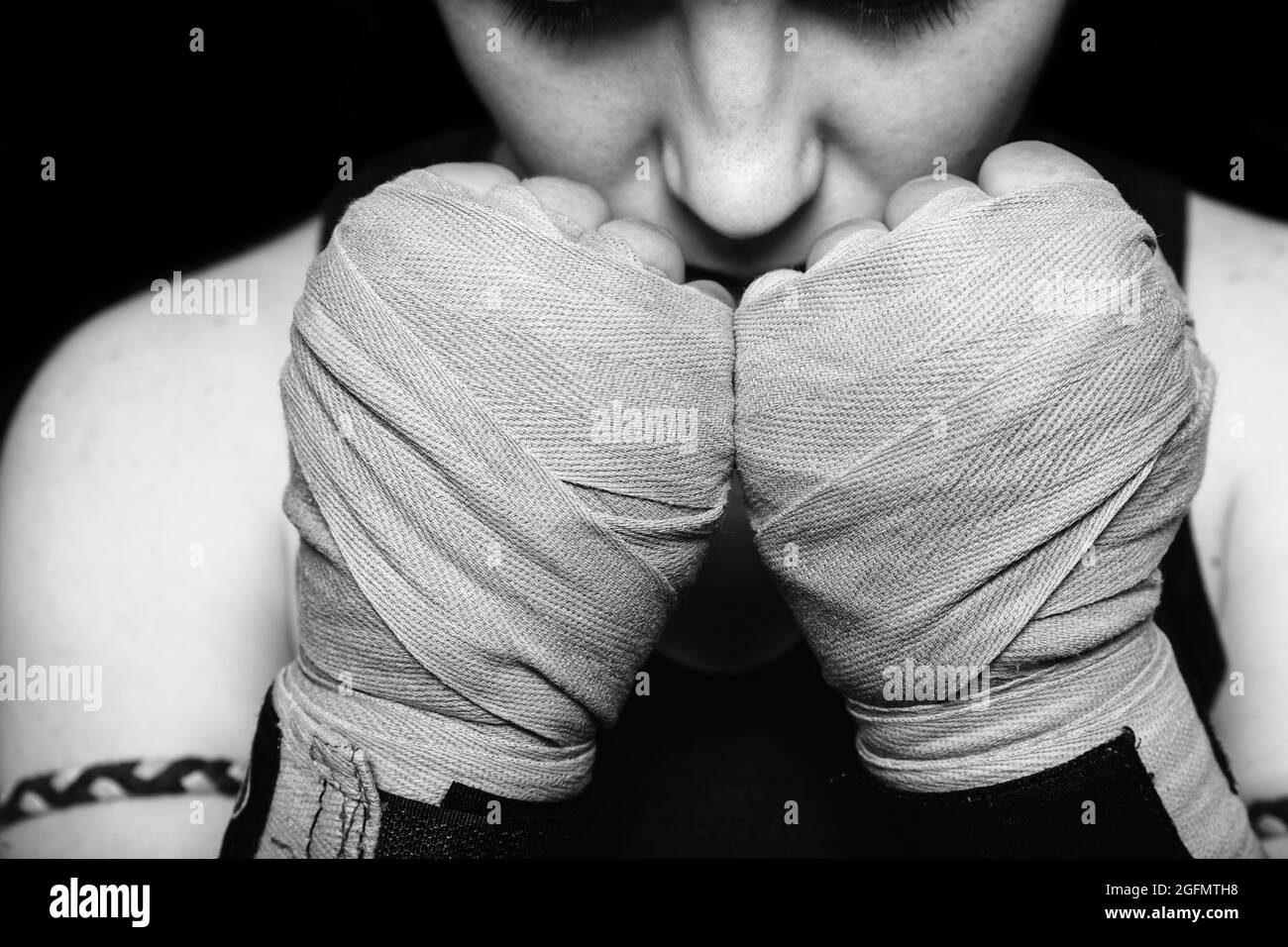 Muay Thai fighter girl preparing for battle. Closeup black and white portrait against black background. Stock Photo