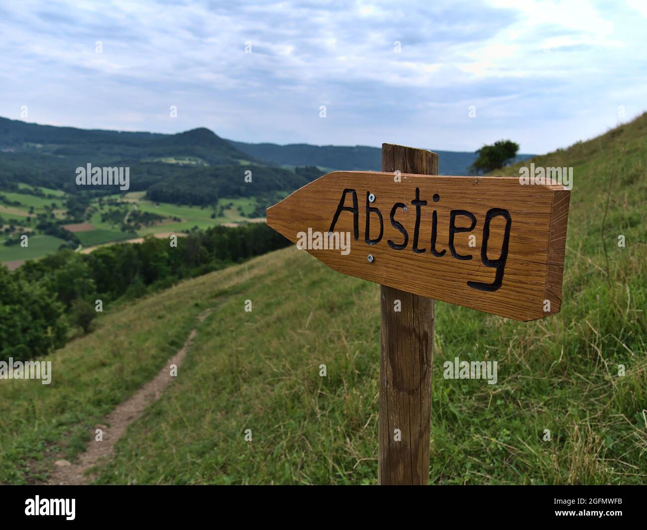 Closeup view of brown wooden sign with German text 'Abstieg' (descent) carved in the wood with hiking path on the slope of Limburg hill, Germany. Stock Photo