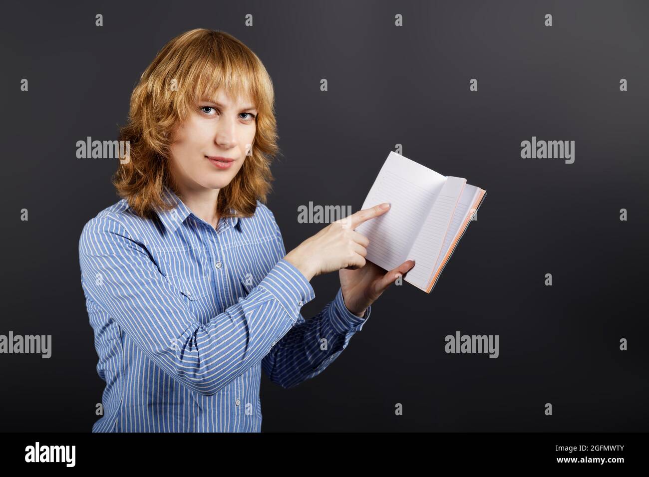A young woman holds a notebook in one hand and pointing to a blank ...