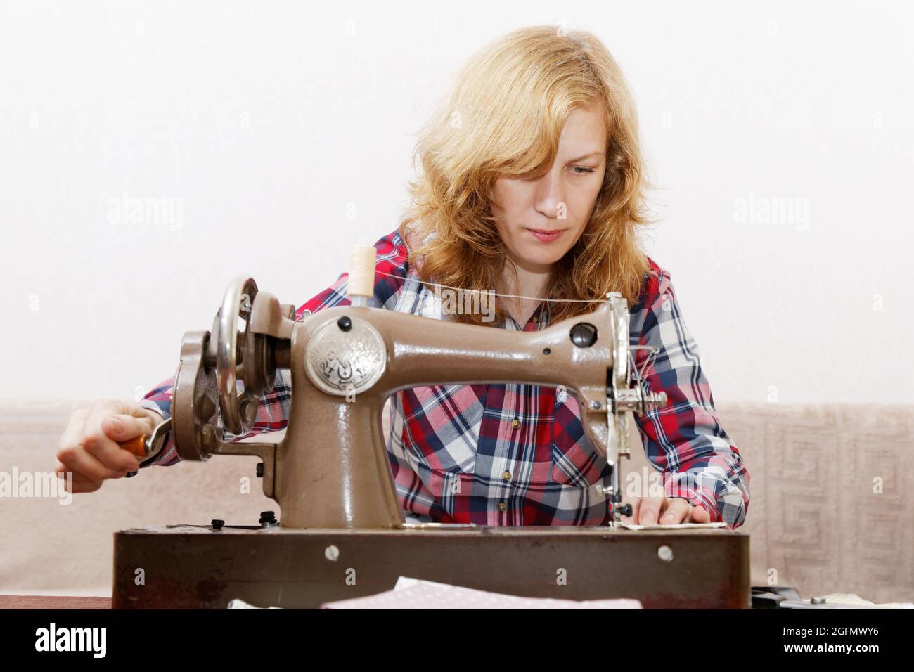 Young red-haired woman stitching fabric using a old vintage sewing machine Stock Photo