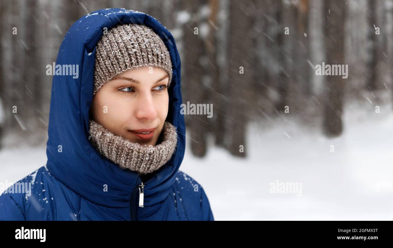 Portrait of a young woman surrounded by flying snowflakes on the background of a winter forest. Shallow focus. Stock Photo